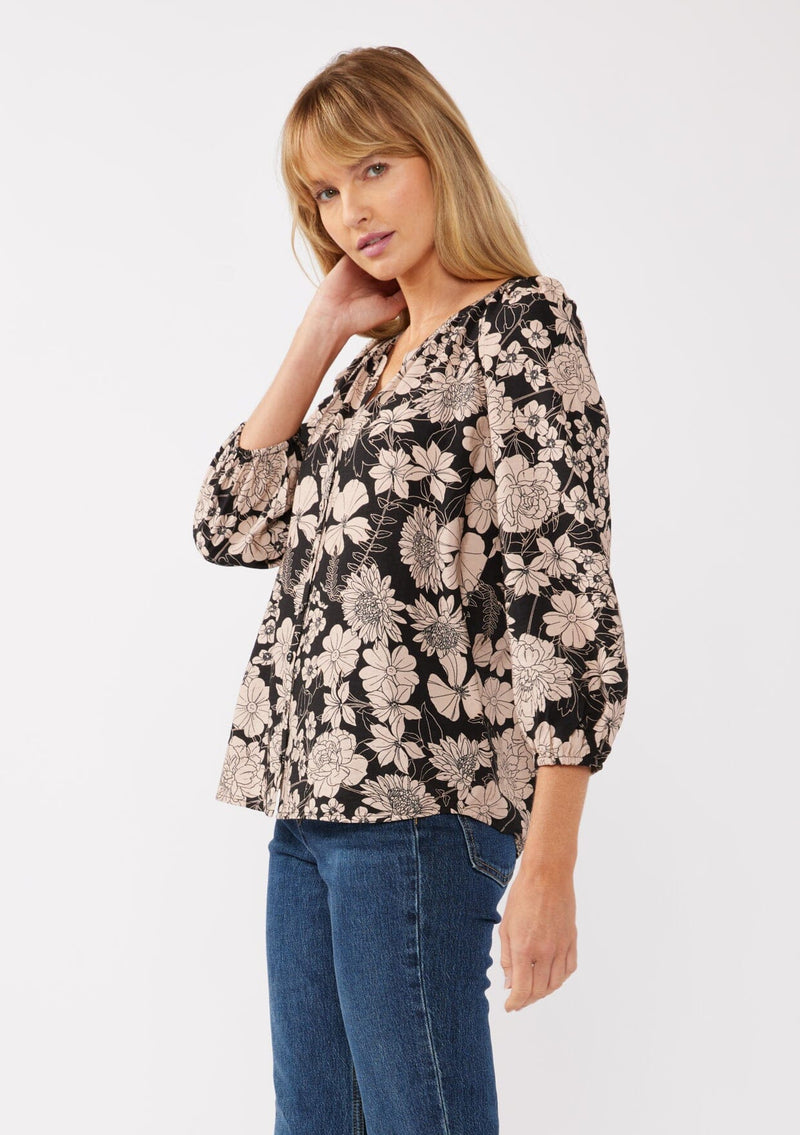 [Color: Black/Taupe] A side facing image of a blonde model wearing a black and taupe floral print blouse. This boho casual blouse features a self covered button front, a split v-neckline, and 3/4 length sleeves. Perfect for any casual outing or vacation. 