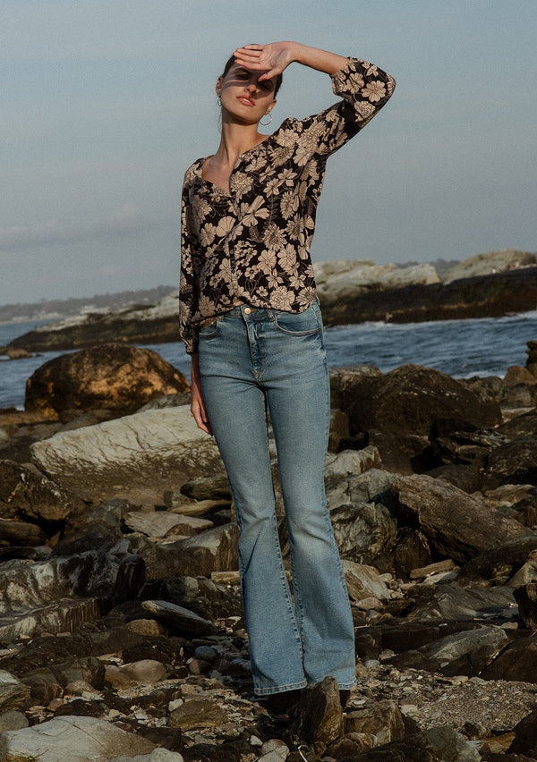 [Color: Black/Taupe] A front facing image of a brunette model wearing a black and taupe floral print blouse near the ocean. This boho casual blouse features a self covered button front, a split v-neckline, and 3/4 length sleeves. Perfect for any casual outing or vacation. 