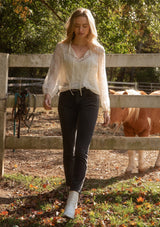 [Color: Ivory] A front facing image of a blonde model wearing a crinkled sheer chiffon blouse with a floral pattern in ivory off white. This relaxed fit blouse features a double tie neck detail, long sleeves with ruffled elastic cuffs, and a detachable cami. 