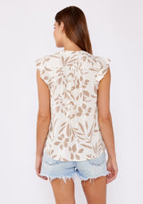 [Color: Latte/Natural] A brunette model wearing a bohemian neutral leaf print top. This casual top features a flutter cap sleeve, shirred yoke, and a v neckline with tassel ties. A summer chic blouse perfectly paired with denim shorts.