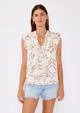 [Color: Latte/Natural] A brunette model wearing a bohemian neutral leaf print top. This casual top features a flutter cap sleeve, shirred yoke, and a v neckline with tassel ties. A summer chic blouse perfectly paired with denim shorts.