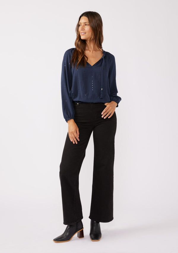 [Color: Midnight] A front facing image of a brunette model wearing a sparkly sequin stripe top in navy blue. Featuring a split v neckline with tassel ties, long sleeves, and a comfortable elastic waistline. Styled dark denim for the fall season.