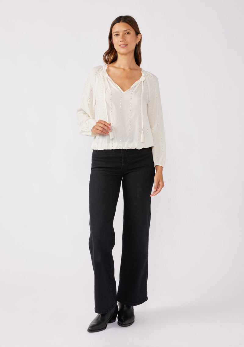 [Color: Natural/Gold] A front facing image of a brunette model wearing a sparkly sequin strip top in ivory off white. Featuring a split v neckline with tassel ties, long sleeves, and a comfortable elastic waistline. Styled for the fall season with black denim jeans and boots. 