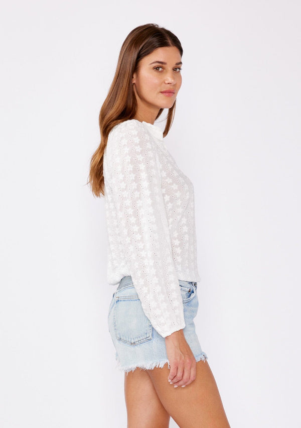 [Color: White] A brunette model wearing a pretty floral embroidered top with eyelet details. A summer breezy top with a ruffled split v neckline and long sleeves with an elastic cuff. An everyday white top styled with cut off denim shorts for summer.