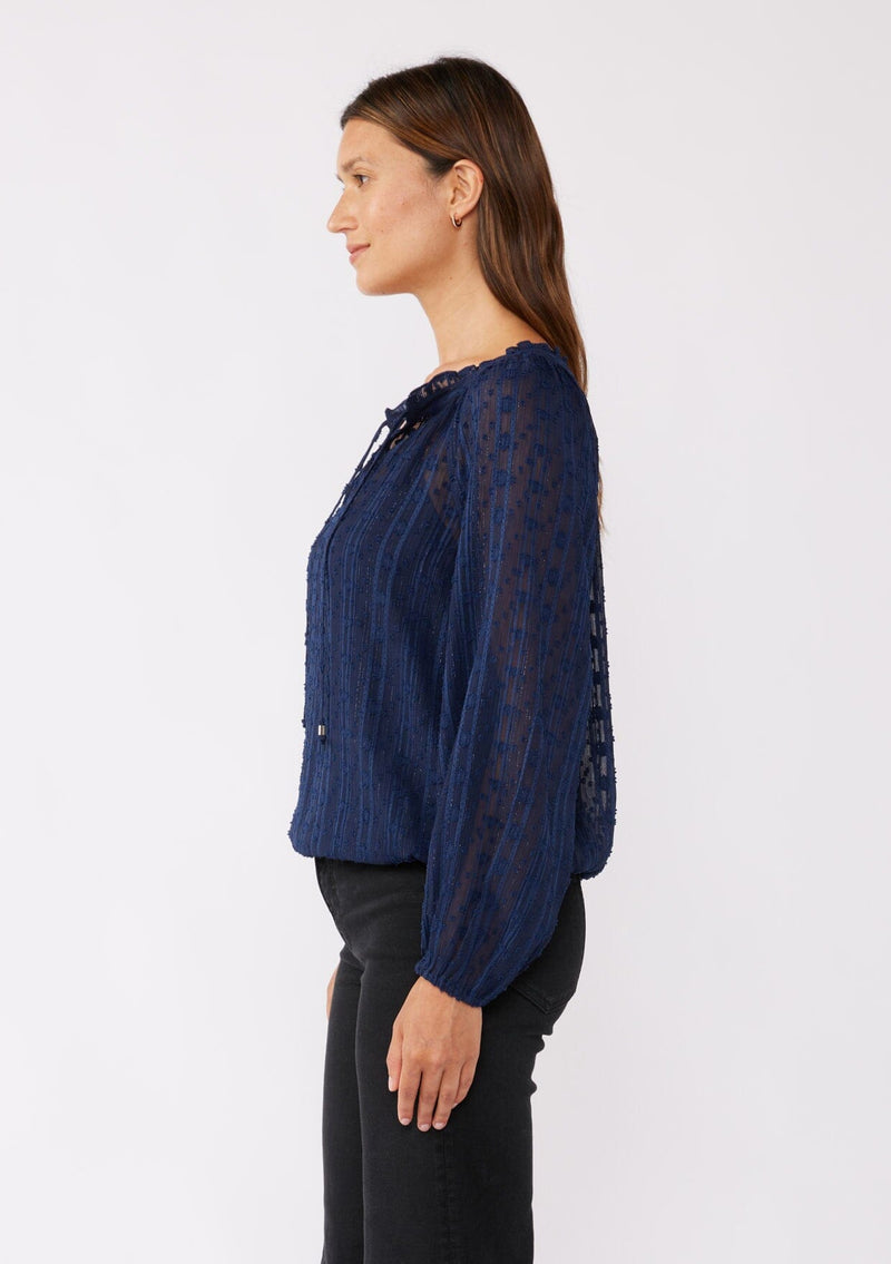 [Color: Navy] A brunette model wearing a navy shimmer blouse crafted on textured chiffon. With a split v neckline with ties, long sleeves, and an elastic hem. The perfect special occasion blouse for formal events or holidays.   