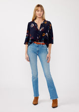 [Color: Navy/Mustard] A front facing image of a blonde model wearing a bohemian fall blouse in a blue floral print. With long sleeves, a v neckline, a self covered button front, and a relaxed fit. 