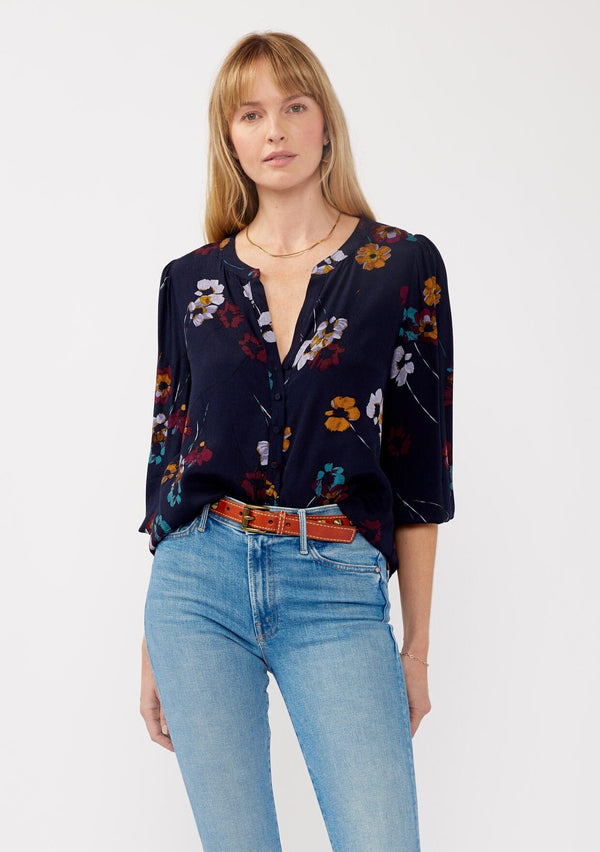 [Color: Navy/Mustard] A front facing image of a blonde model wearing a bohemian fall blouse in a blue floral print. With long sleeves, a v neckline, a self covered button front, and a relaxed fit. 