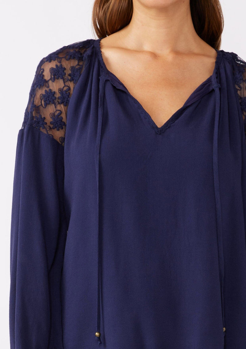 [Color: Navy] A detailed image of a brunette model wearing a navy blue bohemian fall blouse with long sleeves, a split v neckline with ties, and sheer embroidered mesh detail along the shoulders.