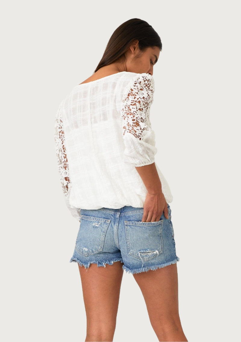 [Color: Off White] A back facing image of a brunette model wearing a white cotton bohemian blouse designed in a textured dobby plaid. With three quarter length crochet sleeves, a v neckline, a self covered button front, and an elastic waist. 