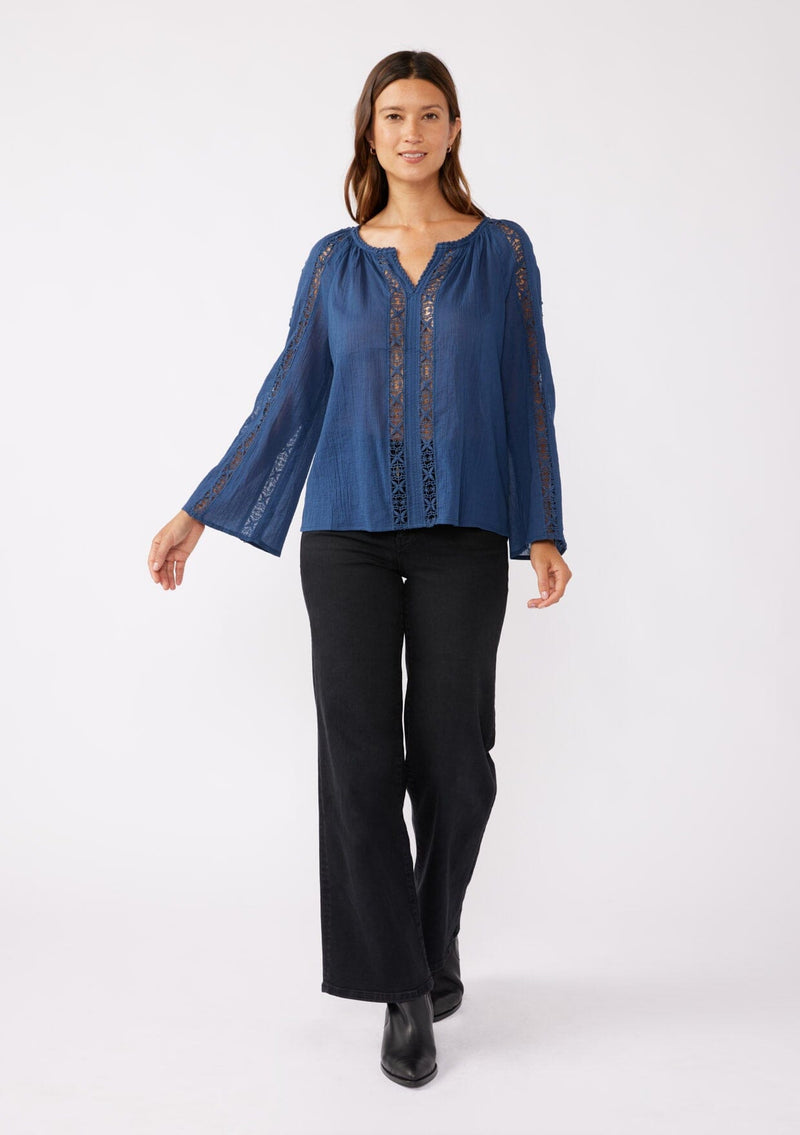 [Color: Blue Indigo] A full body front facing image of a brunette model wearing a classic bohemian blue cotton blouse. With crochet trim, a split v neckline, and long bell sleeves. 