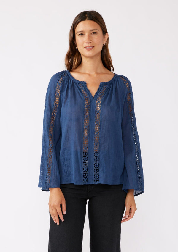 [Color: Blue Indigo] A front facing image of a brunette model wearing a classic bohemian blue cotton blouse. With crochet trim, a split v neckline, and long bell sleeves. 