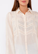 [Color: Light Peach] An image of a brunette model wearing a sheer nude peach color bohemian shirt. With long sleeves, a collared neckline, a self covered button front, and lace trim.