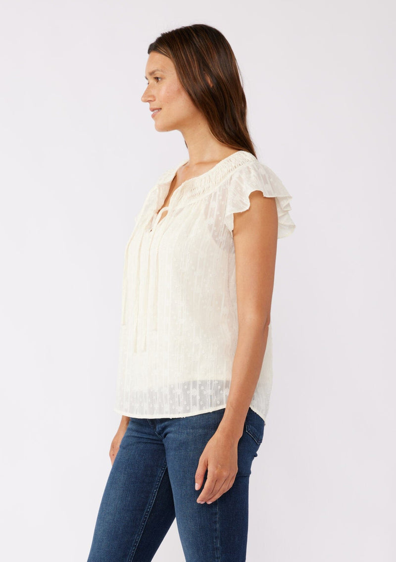 [Color: Ivory] A brunette model wearing a feminine textured chiffon top with metallic striped details. Perfect for the holidays, this ivory off white top features flirty flutter cap sleeves, a split v neckline with ties, and a shirred yoke for definition. An evening top designed for the fall season. 