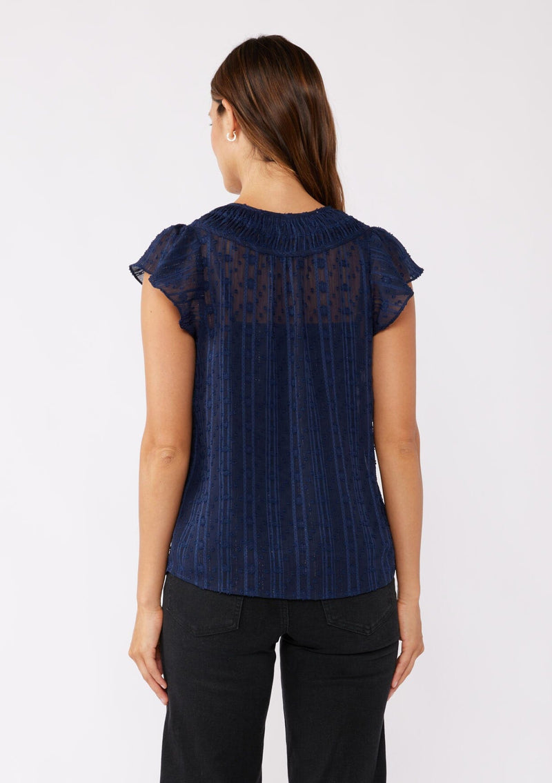 [Color: Navy] A brunette model wearing a feminine textured chiffon top with metallic striped details. Perfect for the holidays, this navy top features flirty flutter cap sleeves, a split v neckline with ties, and a shirred yoke for definition. An evening top designed for the fall season. 