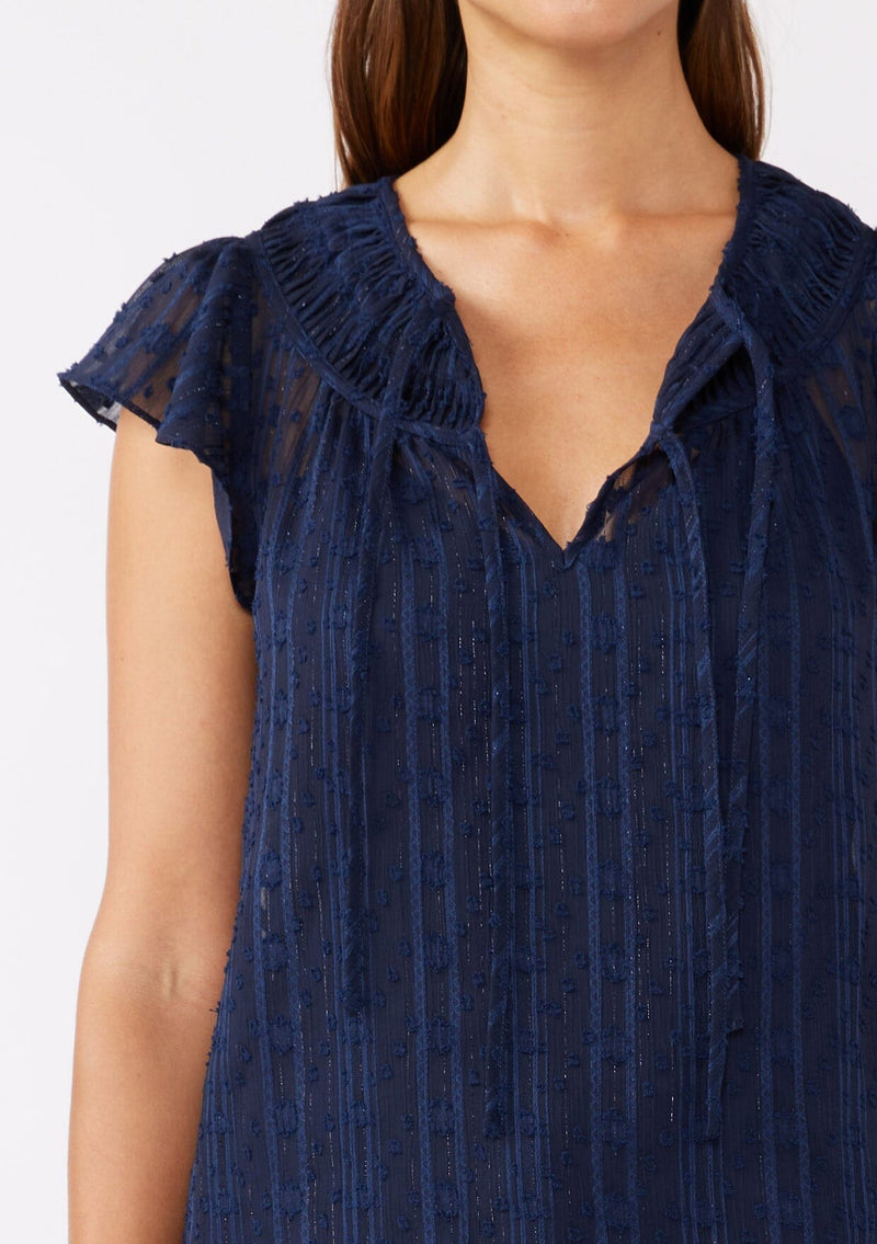 [Color: Navy] A detailed image of a brunette model wearing a feminine textured chiffon top with metallic striped details. Perfect for the holidays, this navy top features flirty flutter cap sleeves, a split v neckline with ties, and a shirred yoke for definition. An evening top designed for the fall season. 