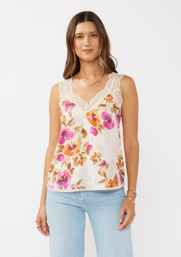 [Color: Natural/Orchid] A front facing image of a brunette model wearing a pretty lace trim cami tank top. A floral print tank with a v neckline, racerback, and  relaxed fit. Styled with light denim jeans for the perfect chic look. 