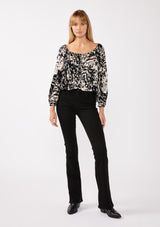 [Color: Black/Blush] A front facing image of a blonde model wearing a bohemian black and white abstract print blouse. Featuring an elastic scoop neckline, tie front detail, long sleeves with cuffs, and a relaxed fit. Perfect for any casual outing whether paired with shorts or long bottoms. 