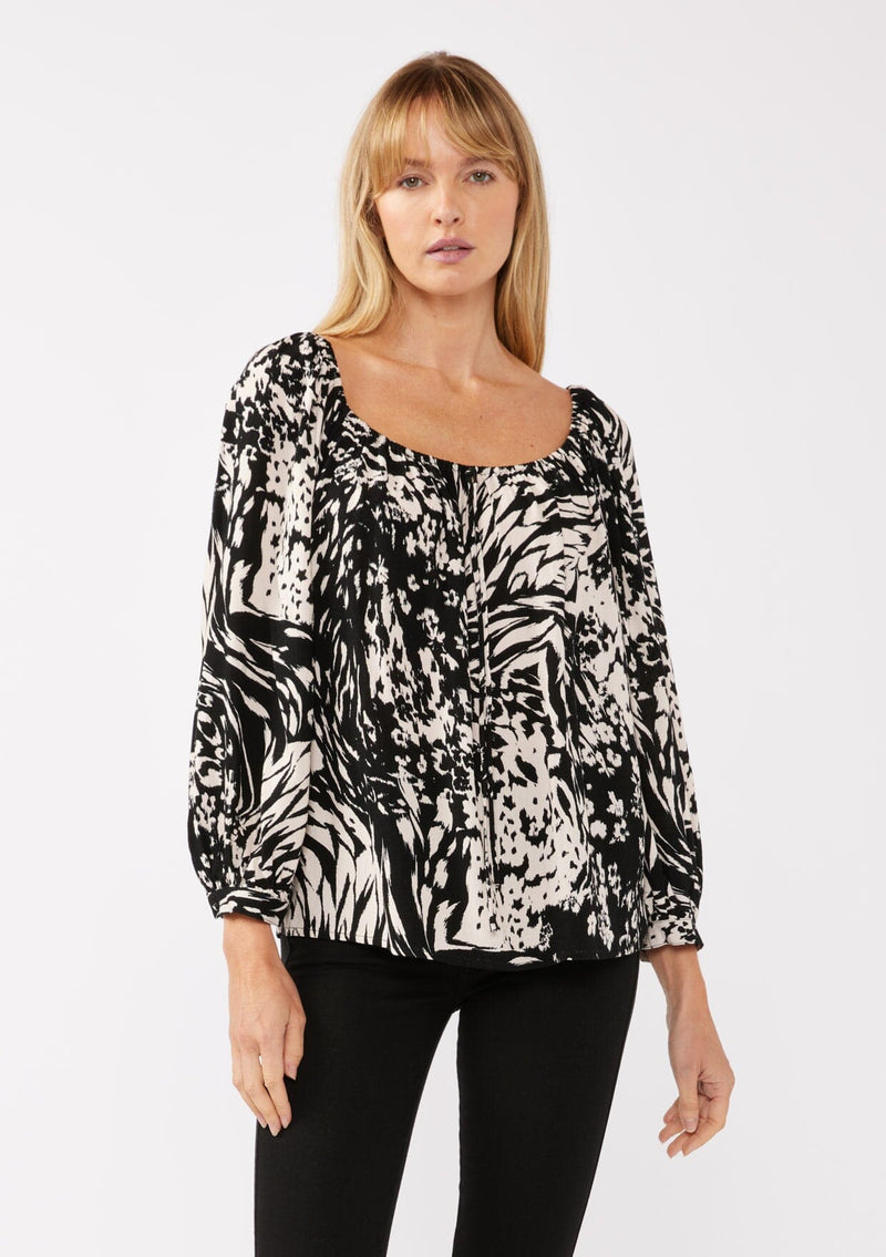 [Color: Black/Blush] A front facing image of a blonde model wearing a bohemian black and white abstract print blouse. Featuring an elastic scoop neckline, tie front detail, long sleeves with cuffs, and a relaxed fit. Perfect for any casual outing whether paired with shorts or long bottoms. 