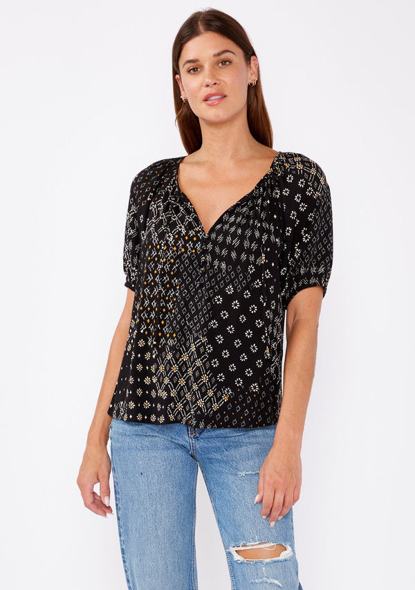 [Color: Black/Gold] A brunette model wearing a fall bohemian mixed floral print blouse with a split v neckline with ties and short buff sleeves. Features a partial button front for easy styling. A pretty fall top paired with denim jeans for a casual look. 