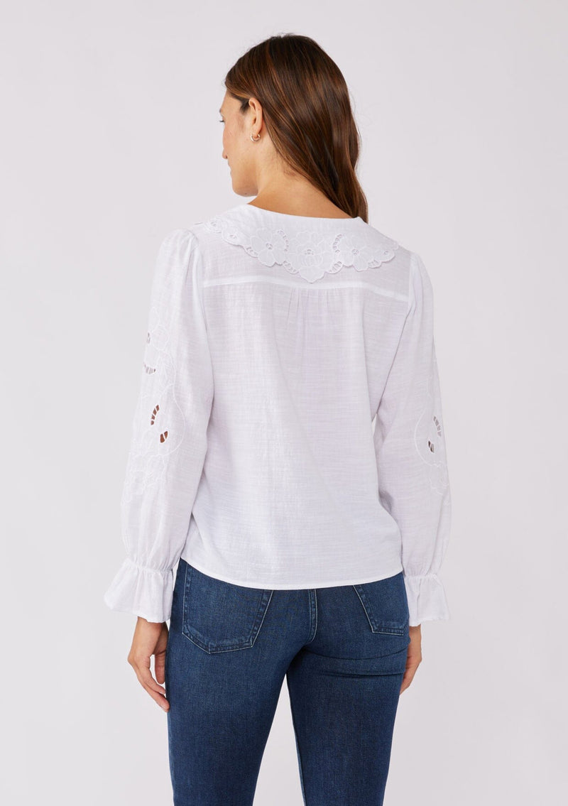 [Color: White] A back facing image of a brunette model wearing a white blouse with a peter pan collar. A relaxed fit bohemian blouse with tonal embroidery, hook and eye front closure, long sleeves, and ruffle trim cuffs.