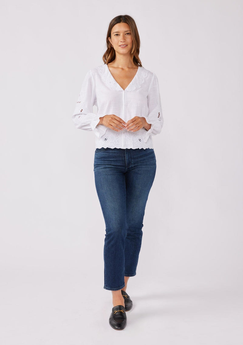 [Color: White] A full body image of a brunette model wearing a white blouse with a peter pan collar. A relaxed fit bohemian blouse with tonal embroidery, hook and eye front closure, long sleeves, and ruffle trim cuffs.