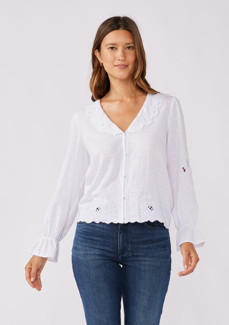 [Color: White] A front facing image of a brunette model wearing a white blouse with a peter pan collar. A relaxed fit bohemian blouse with tonal embroidery, hook and eye front closure, long sleeves, and ruffle trim cuffs.