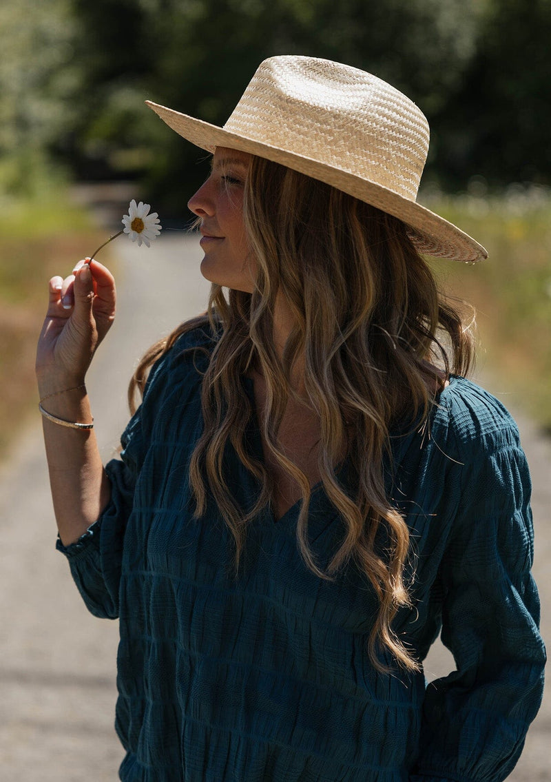 [Color: Deep Teal] A blonde model wearing a textured jacquard stripe blouse in teal. A relaxed fit blouse with a split v neckline and long sleeves. Styled with loose fit denim jeans.