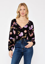 [Color: Black/Purple] A blonde model wearing a flowy bohemian top in a black and purple floral print. Featuring long sleeves with pintuck details and a split v neckline with ties. A casual, everyday top, perfect for any occasion during the Fall season. 