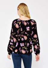 [Color: Black/Purple] A blonde model wearing a flowy bohemian top in a black and purple floral print. Featuring long sleeves with pintuck details and a split v neckline with ties. A casual, everyday top, perfect for any occasion during the Fall season. 