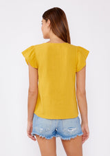 [Color: Mustard] An image of a brunette model wearing a mustard yellow top crafted from cotton gauze. With short flutter sleeves and v neckline. A comfortable top for the summer to fall season that can be paired with denim shorts and pants.
