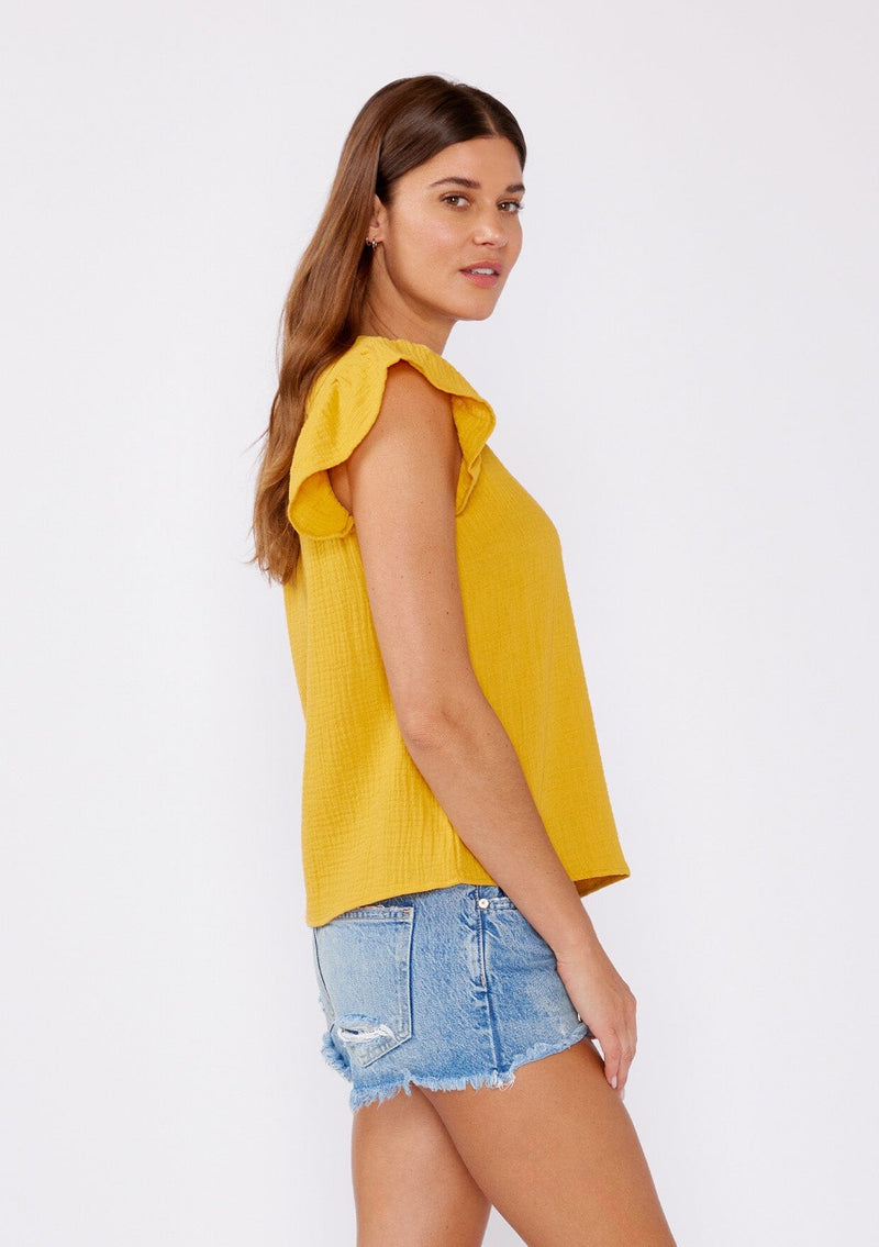 [Color: Mustard] An image of a brunette model wearing a mustard yellow top crafted from cotton gauze. With short flutter sleeves and v neckline. A comfortable top for the summer to fall season that can be paired with denim shorts and pants.