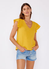 [Color: Mustard] An image of a brunette model wearing a mustard yellow top crafted from cotton gauze. With short flutter sleeves and v neckline. A comfortable top for the summer to fall season that can be paired with denim shorts and pants. 