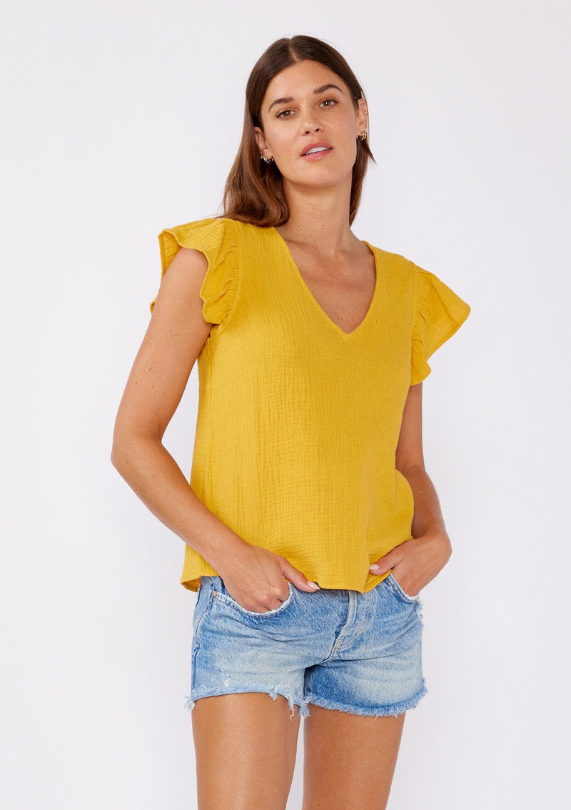 [Color: Mustard] An image of a brunette model wearing a mustard yellow top crafted from cotton gauze. With short flutter sleeves and v neckline. A comfortable top for the summer to fall season that can be paired with denim shorts and pants. 