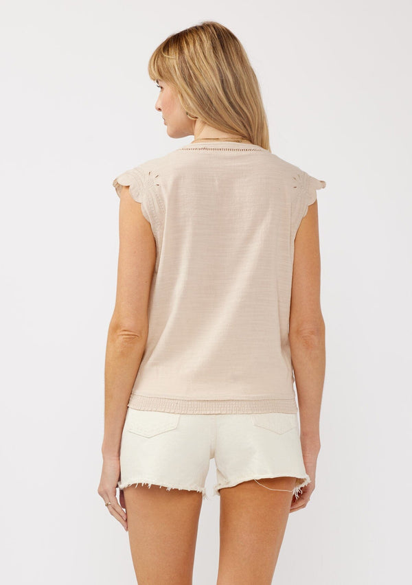 [Color: Buff] A back facing image of a blonde model wearing a taupe rayon and cotton blend top with an embroidered floral cutout design. This casual spring top features a v neckline, button front, short dolman sleeves, and a hip hugging elastic hem at the back. 