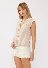 [Color: Buff] A side facing image of a blonde model wearing a taupe rayon and cotton blend top with an embroidered floral cutout design. This casual spring top features a v neckline, button front, short dolman sleeves, and a hip hugging elastic hem at the back. 