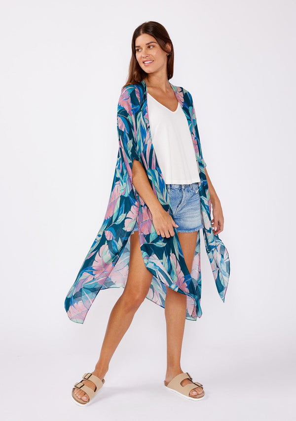 [Color: Teal/Dusty Orchid] A brunette model wearing a blue and pink tropical inspired palm leaf print kimono. A lightweight kimono perfect for the beach or to style a casual outfit. With an open front, mid length , half kimono sleeves, and side vents.