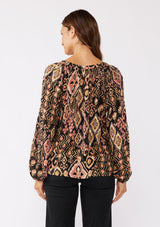 [Color: Grey/Dusty Rose] A back image of a brunette model wearing an ultra boho blouse with geometric ikat print in dusty pink and yellow. A casual fall blouse with a split v-neckline, long sleeves, and a relaxed fit. 