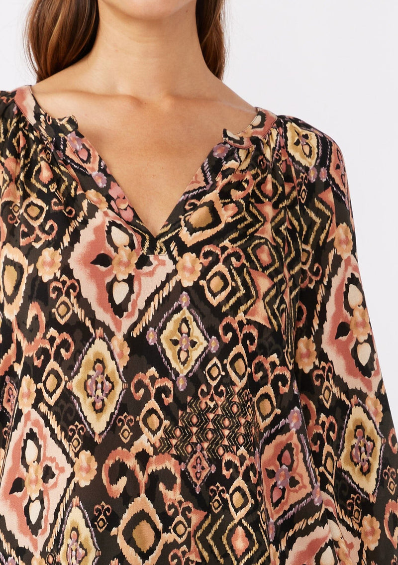 [Color: Grey/Dusty Rose] A detailed image of a brunette model wearing an ultra boho blouse with geometric ikat print in dusty pink and yellow. A casual fall blouse with a split v-neckline, long sleeves, and a relaxed fit. 