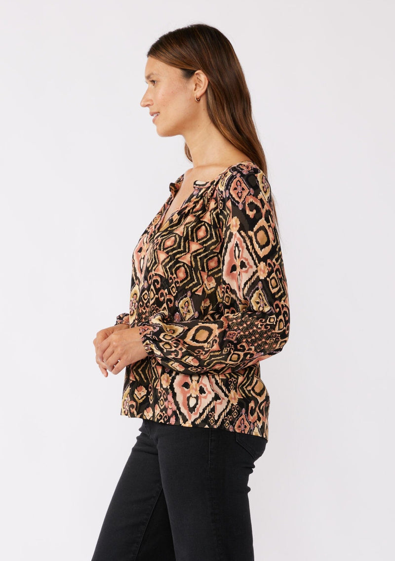 [Color: Grey/Dusty Rose] A side image of a brunette model wearing an ultra boho blouse with geometric ikat print in dusty pink and yellow. A casual fall blouse with a split v-neckline, long sleeves, and a relaxed fit. 