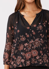 [Color: Black/Dusty Rose] A detail shot of a brunette model wearing a sheer chiffon black blouse with a pink floral print. A lightweight top featuring a button front, split v neckline, and 3/4 length sleeves. Ideal for special occasions and holiday events. 