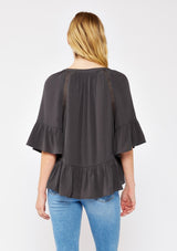 [Color: Charcoal] A blonde model wearing a grey relaxed fit peplum style blouse. A button front top with flutter half sleeves, split v neckline, and lace trim inserts. Styled with light denim jeans for an ultra boho look.