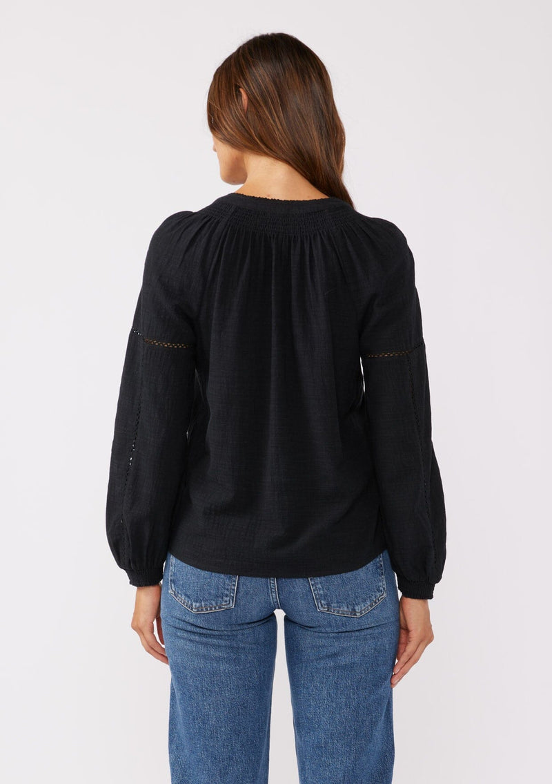 [Color: Black] A front facing image of a brunette model wearing a pretty boho blouse in a black. With floral tonal embroidery, lace trim inserts, long sleeves with smocked wrist cuffs, and a split v neckline. An airy and relaxed fit blouse crafted in a cotton blend fabric.