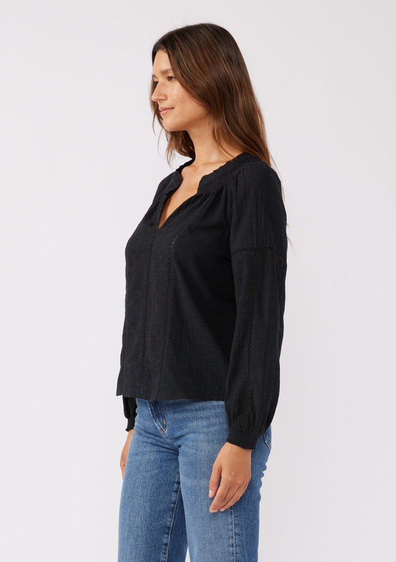 [Color: Black] A front facing image of a brunette model wearing a pretty boho blouse in a black. With floral tonal embroidery, lace trim inserts, long sleeves with smocked wrist cuffs, and a split v neckline. An airy and relaxed fit blouse crafted in a cotton blend fabric.