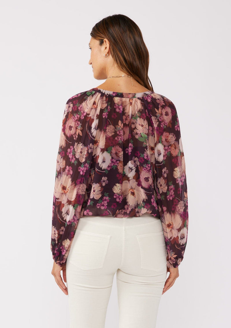 [Color: Plum/Dusty Rose] A back facing brunette model wearing a purple floral chiffon top with pleated long sleeves, button front, split v-neckline, and elastic hem. Perfect for holidays, work events, or date nights.