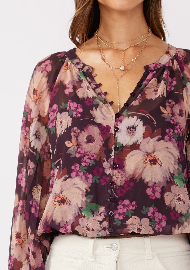 [Color: Plum/Dusty Rose] A detail shot brunette model wearing a purple floral chiffon top with pleated long sleeves, button front, split v-neckline, and elastic hem. Perfect for holidays, work events, or date nights.