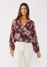 [Color: Plum/Dusty Rose] A brunette model wearing a purple floral chiffon top with pleated long sleeves, button front, split v-neckline, and elastic hem. Perfect for holidays, work events, or date nights.