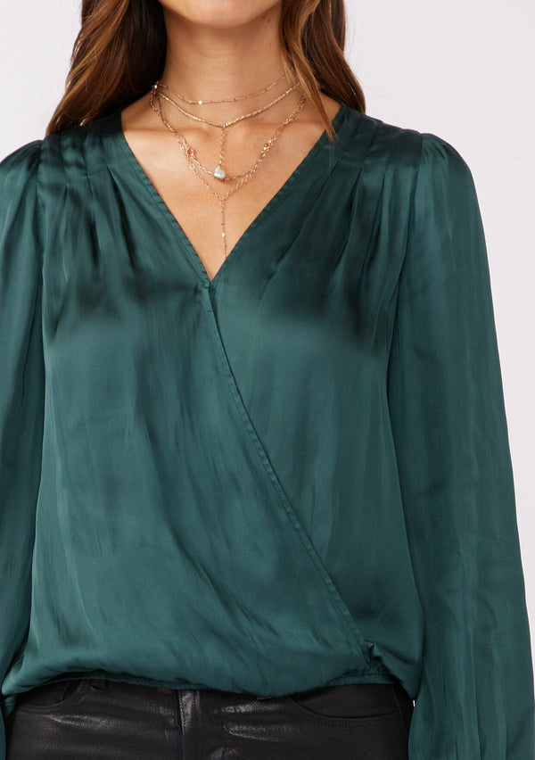 [Color: Teal] A detail image of a brunette model wearing a holiday green silky polyester satin top. This special occasion top features a surplice v neckline, front hook and eye closure, elastic hemline, and long sleeves. Perfect for Christmas and holiday parties. 