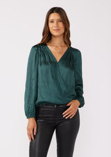 [Color: Teal] A front facing image of a brunette model wearing a holiday green silky polyester satin top. This special occasion top features a surplice v neckline, front hook and eye closure, elastic hemline, and long sleeves. Perfect for Christmas and holiday parties. 