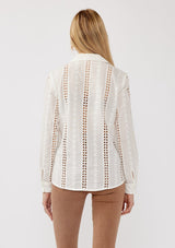 [Color: White] A back facing image of a blonde model wearing floral eyelet shirt with a collared neckline, button front, and long sleeves with button cuffs. A sophisticated spring top paired with brown denim bottoms for spring. 