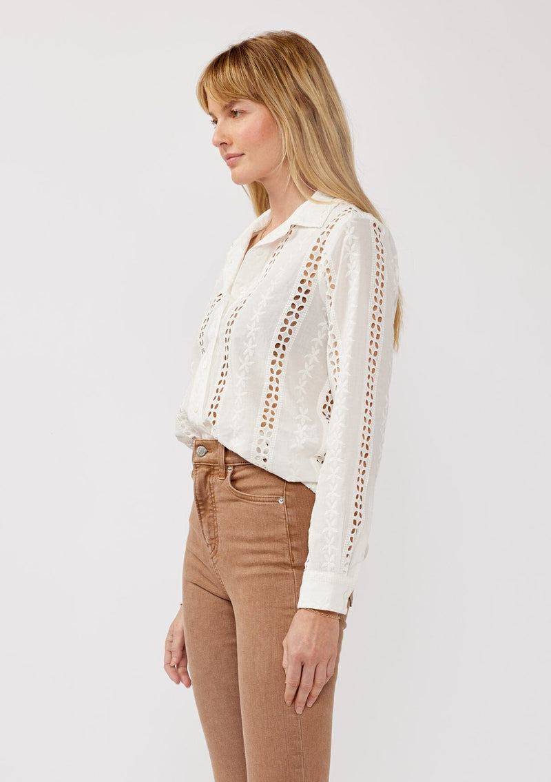 [Color: White] A shit facing image of a blonde model wearing floral eyelet shirt with a collared neckline, button front, and long sleeves with button cuffs. A sophisticated spring top paired with brown denim bottoms for spring. 